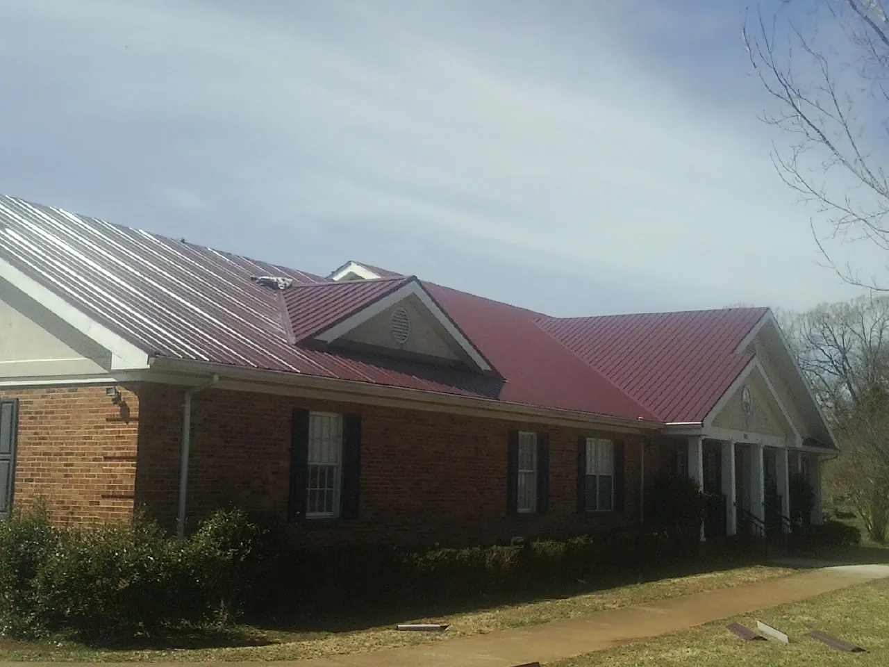 Red metal roof with gabled entries on a long brick building, from a Hail Damage Roof Repair job in Benicia
