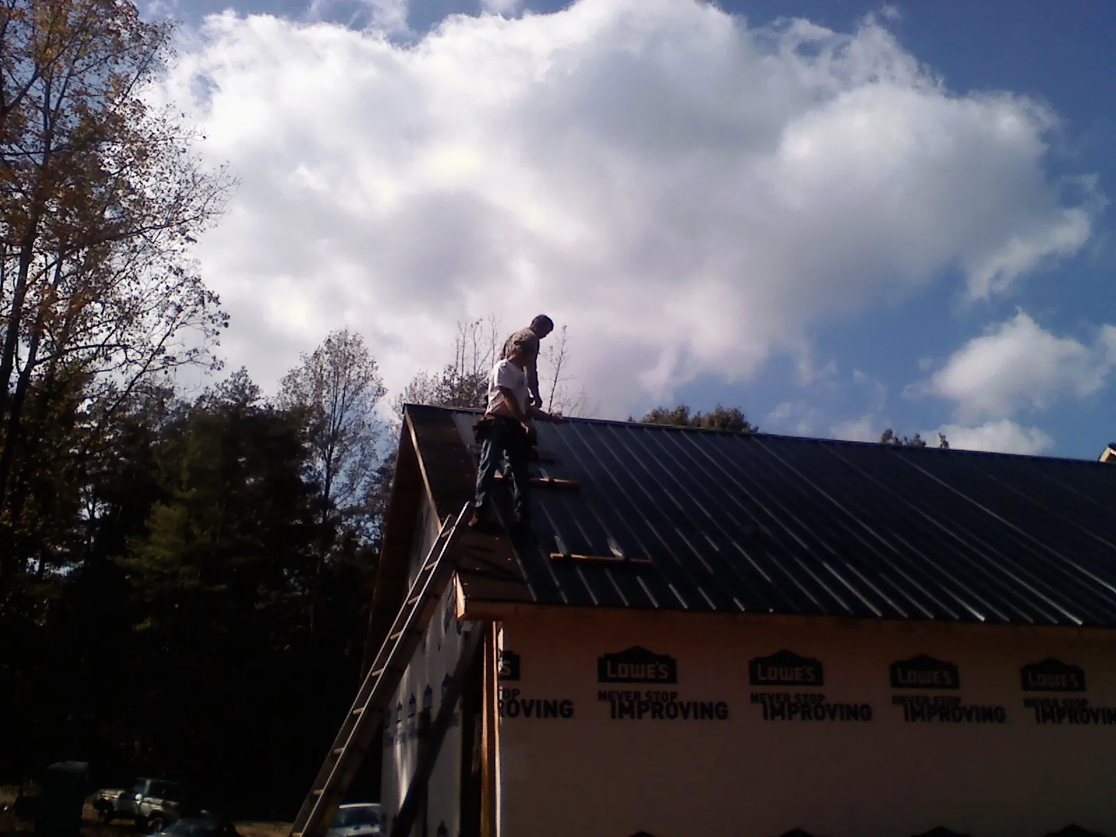 Roofer fastening dark metal panels high against a cloudy sky, from a Roof Inspection job in Benicia